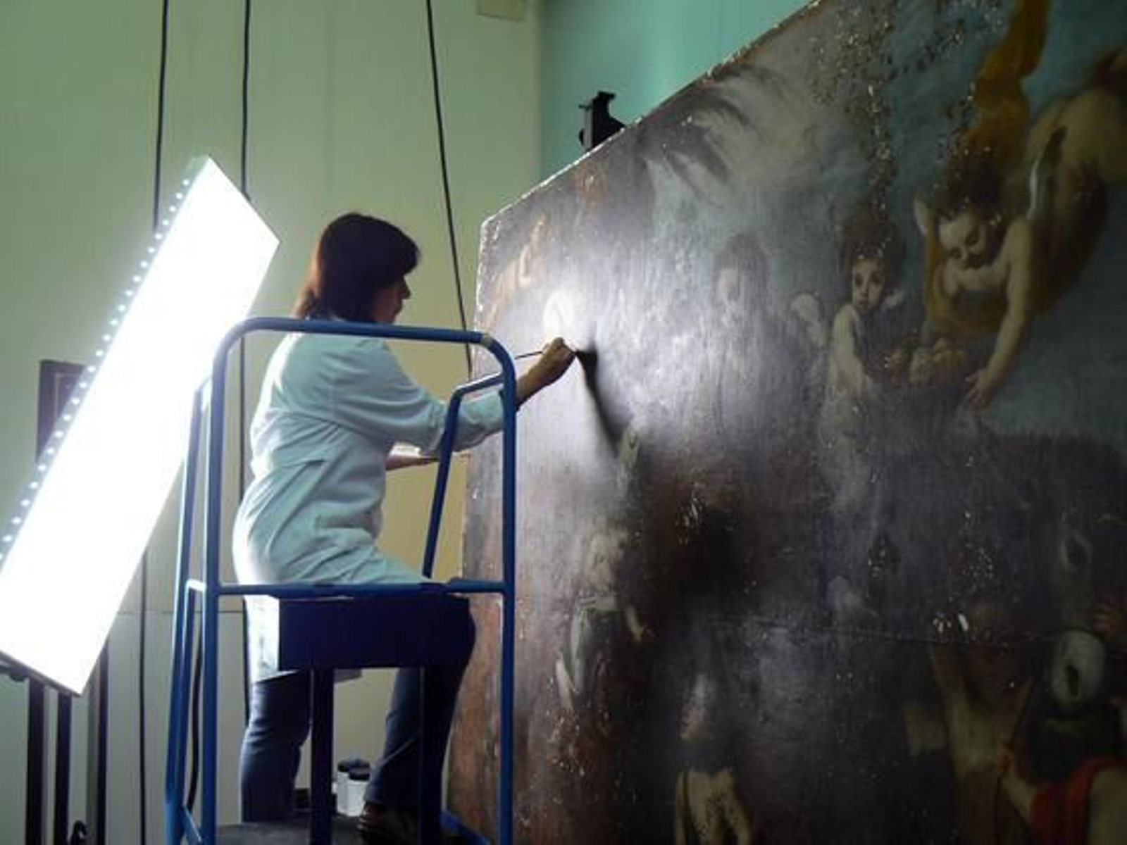 Una restauradora trabaja sobre una tabla subida en una escalera del taller.

Foto: Ruesga Bono