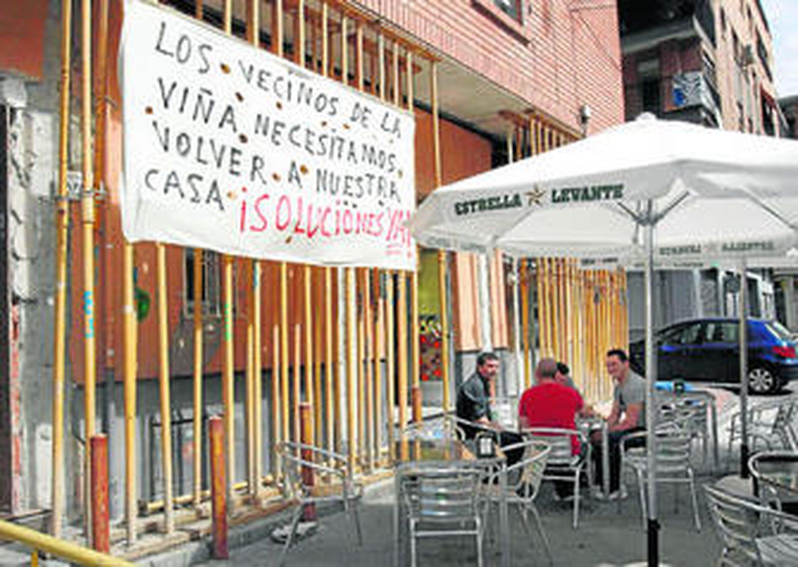 Unos vecinos toman un refresco junto a un edificio todavía apuntalado ante el riesgo de derrumbe.