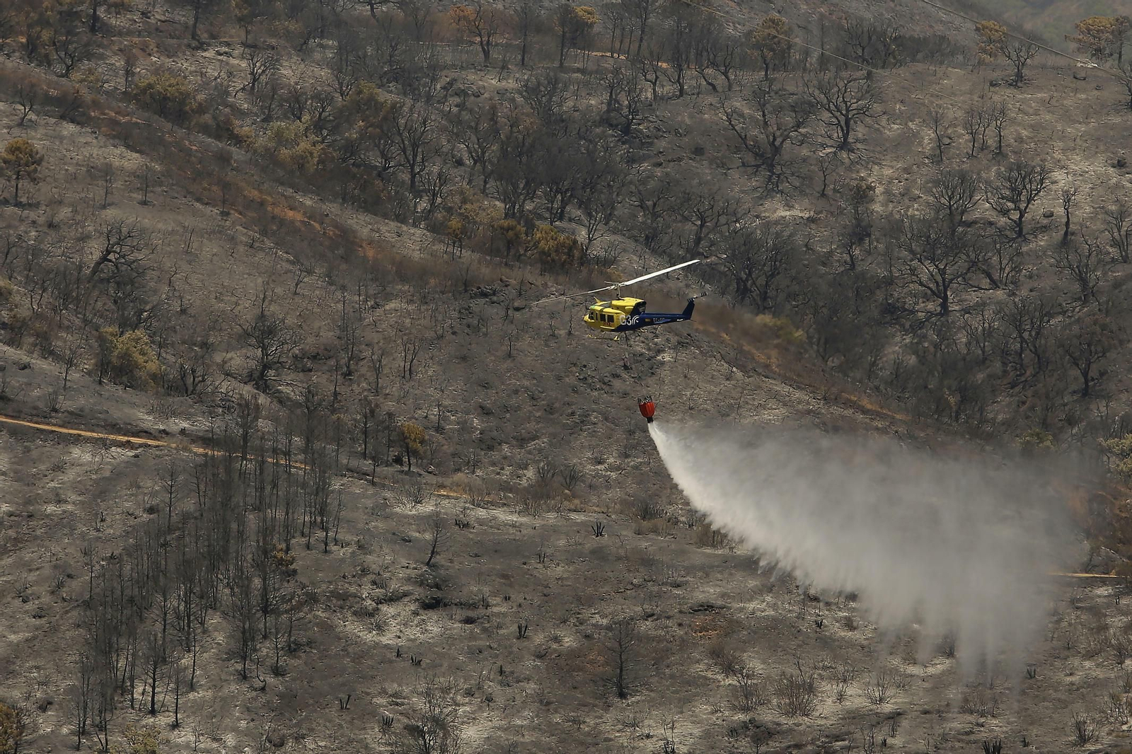 Un helicóptero del Infoca realiza labores de refresco sobre una zona quemada.