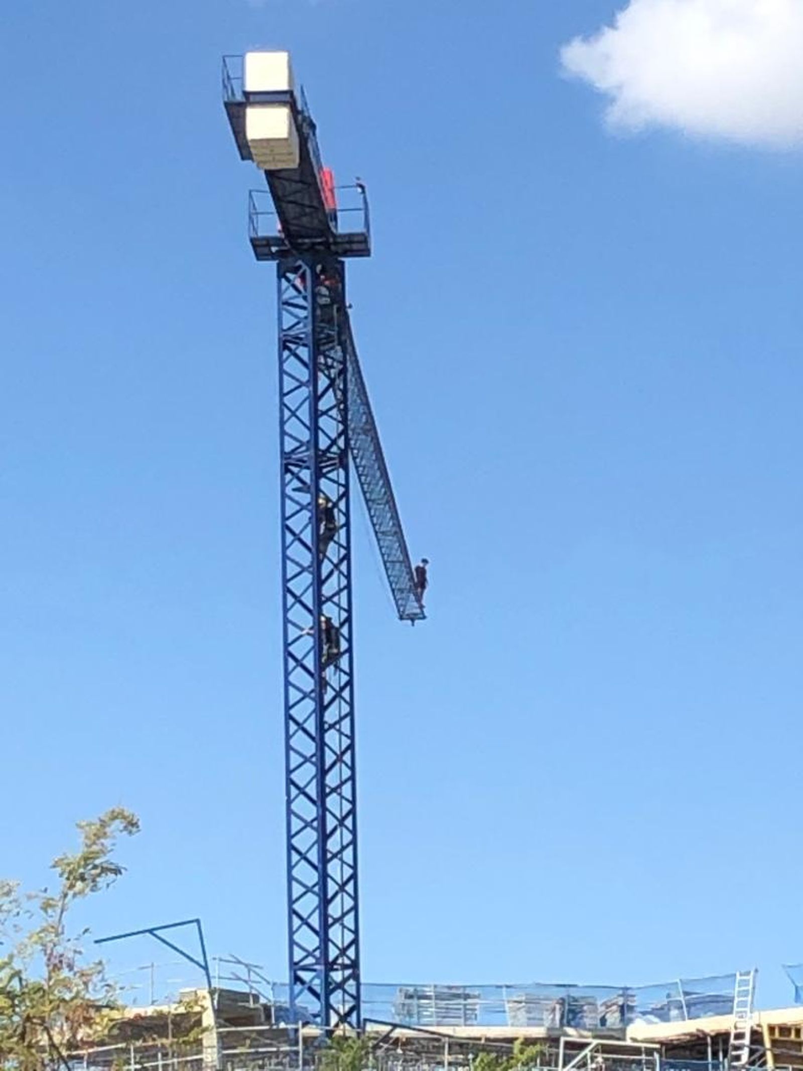 Dos bomberos escalan hacia donde está el joven, en la punta de la grúa.