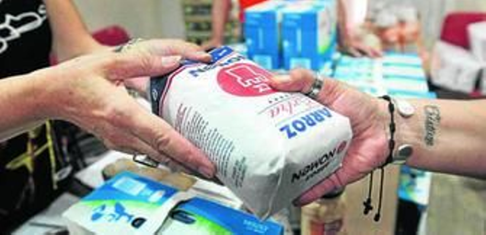 Una voluntaria tiende a un usuario un paquete de arroz que forma parte de la bolsa de alimentos de este mes en el despacho de Valvanuz.
