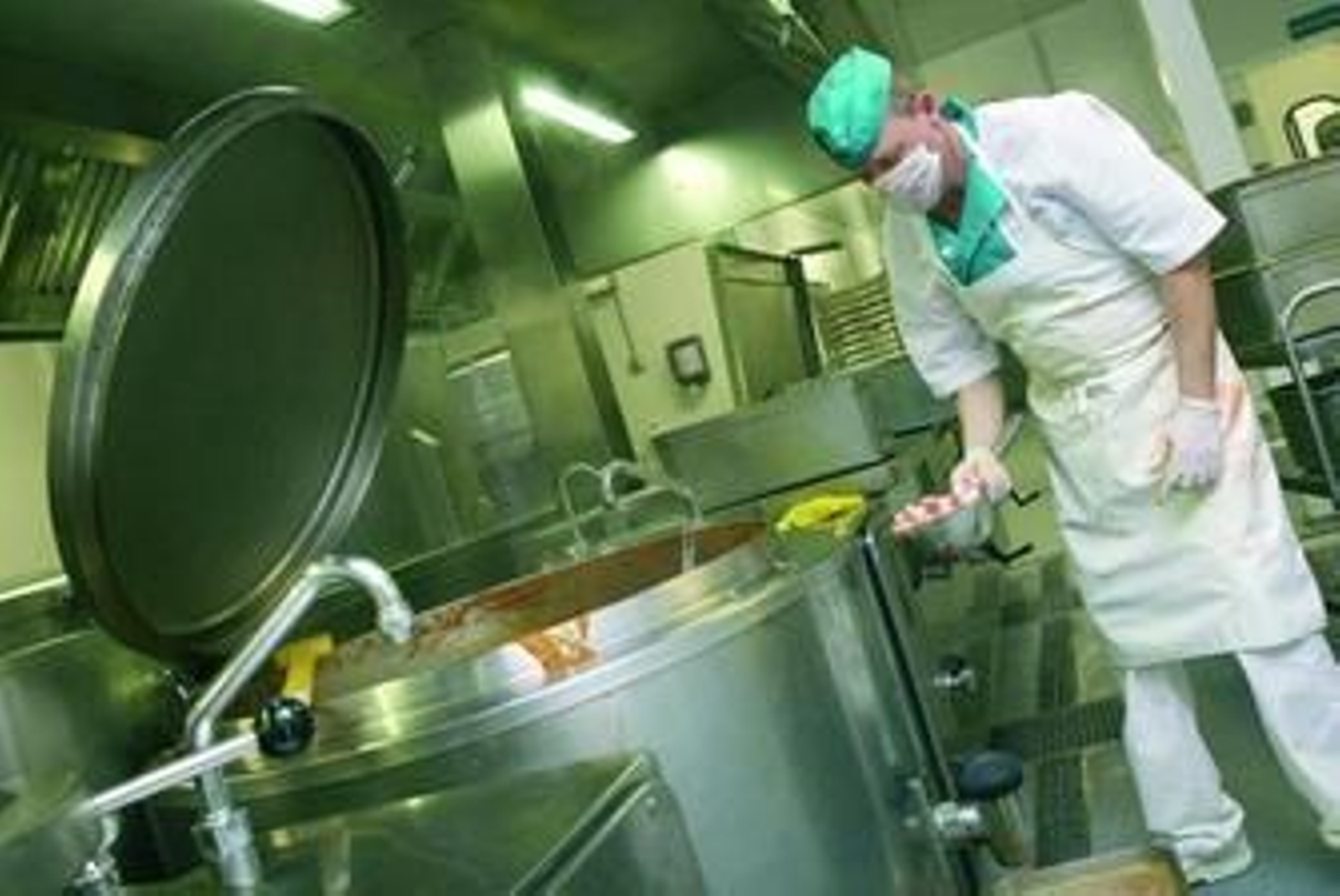 Uno de los cocineros sostiene un cazo de ingredientes para la cazuela de fideos que se cocina en una marmita de 500 litros.