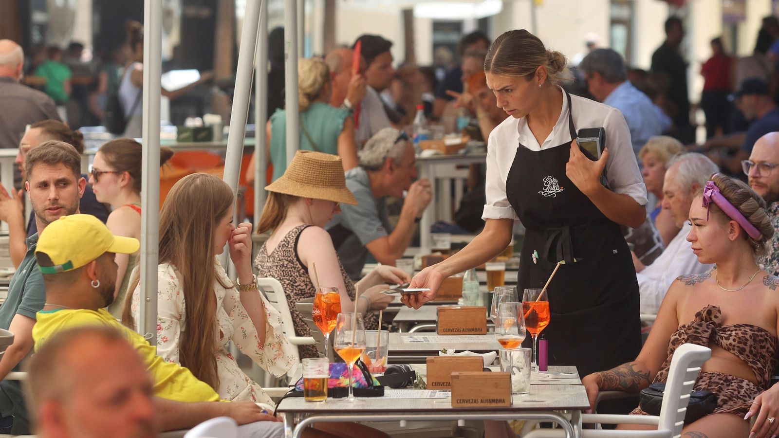 Una camarera cobra a clientes en una terraza de Málaga.