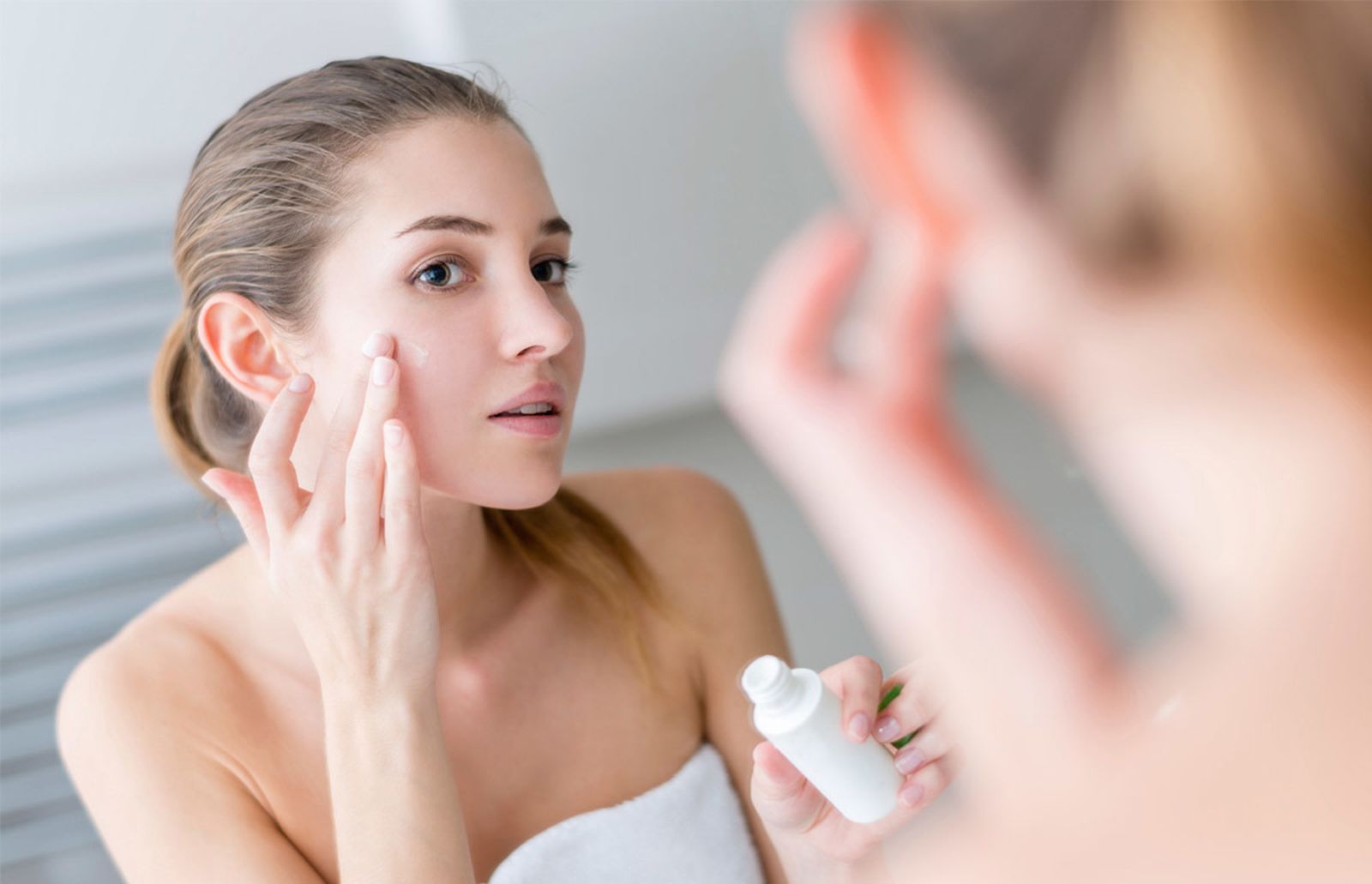 Una joven aplica crema en su rostro después de su rutina de limpieza.