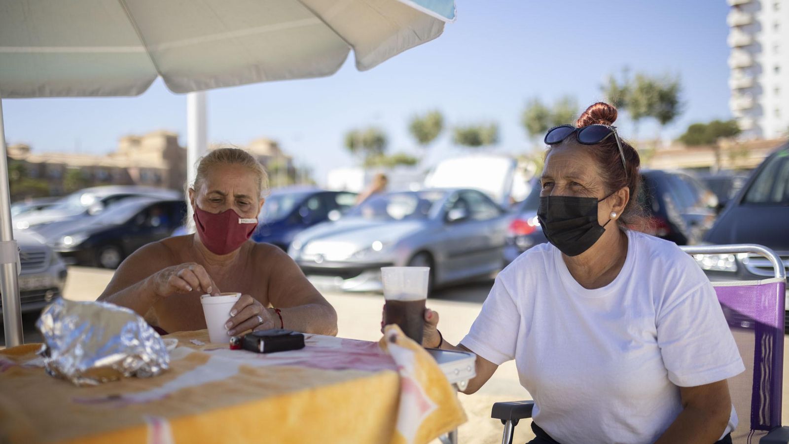 Dos mujeres conversan bajo una sombrilla junto a la playa.