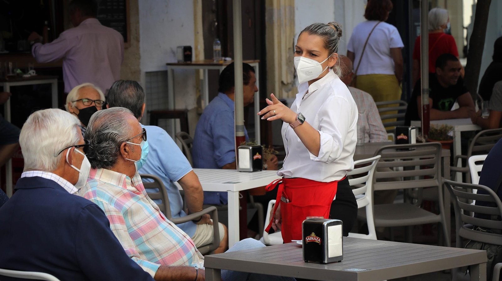 Una camarera atiende a clientes de un bar del centro, todos con la mascarilla puesta.