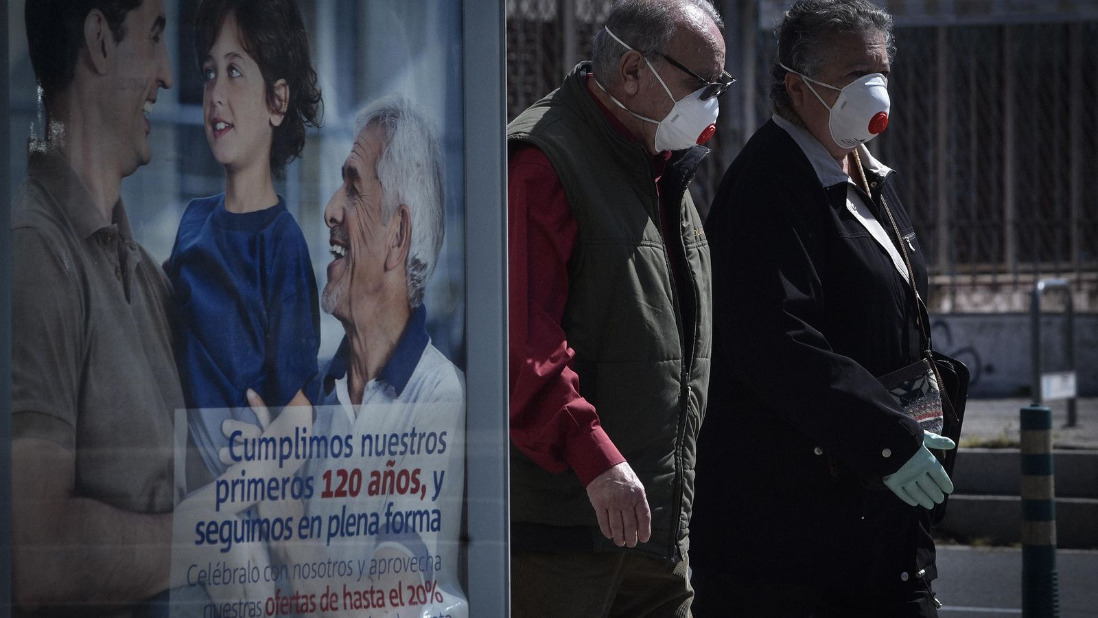 Dos peatones con mascarillas pasan junto a un anuncio publicitario