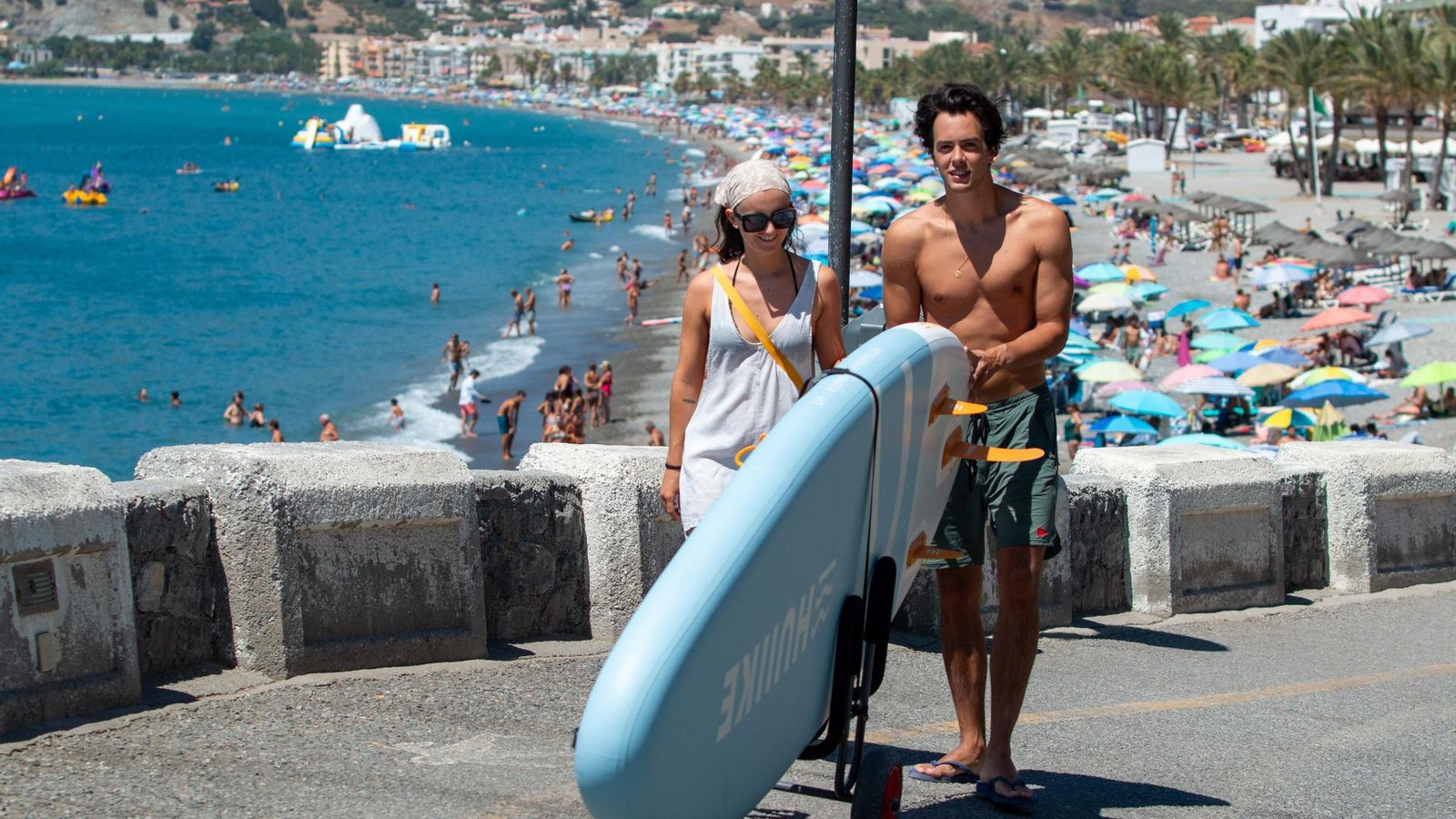 Dos jóvenes cargan con la tabla de paddle surf por La Herradura