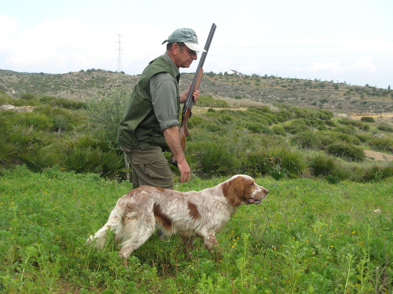 Un cazador avanza por una finca junto a su perro.