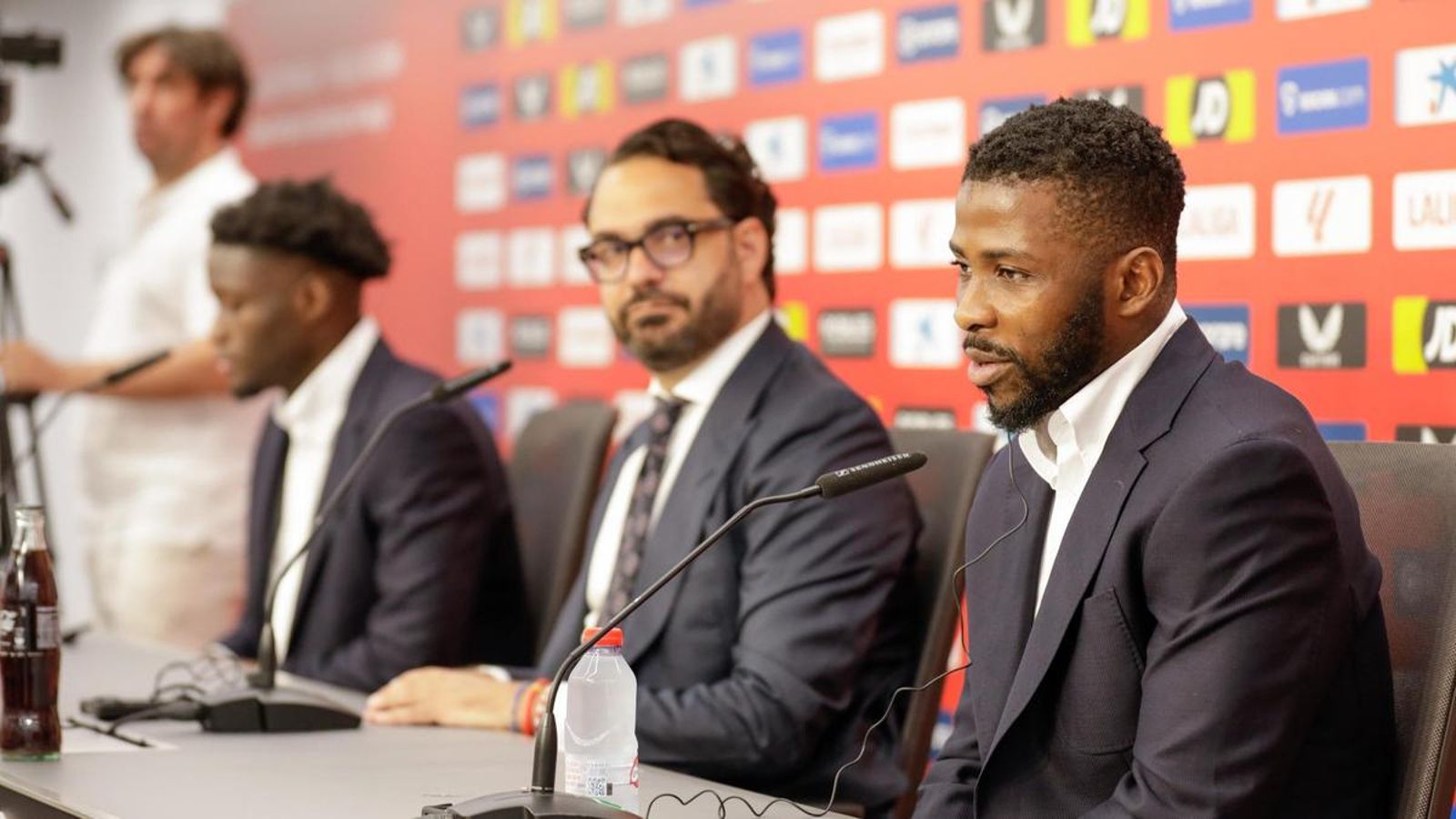 Víctor Orta, en segundo plano con Agoumé, observa a Iheanacho durante su rueda de prensa.
