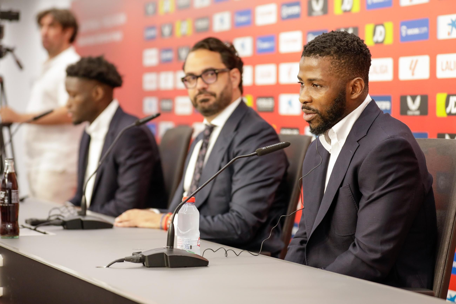 Víctor Orta, en segundo plano con Agoumé, observa a Iheanacho durante su rueda de prensa.