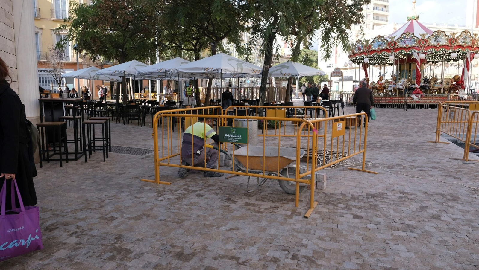 Mesas y sillas de una de las terrazas de Puerta Purchena junto a obras y el tiovivo de Navidad.