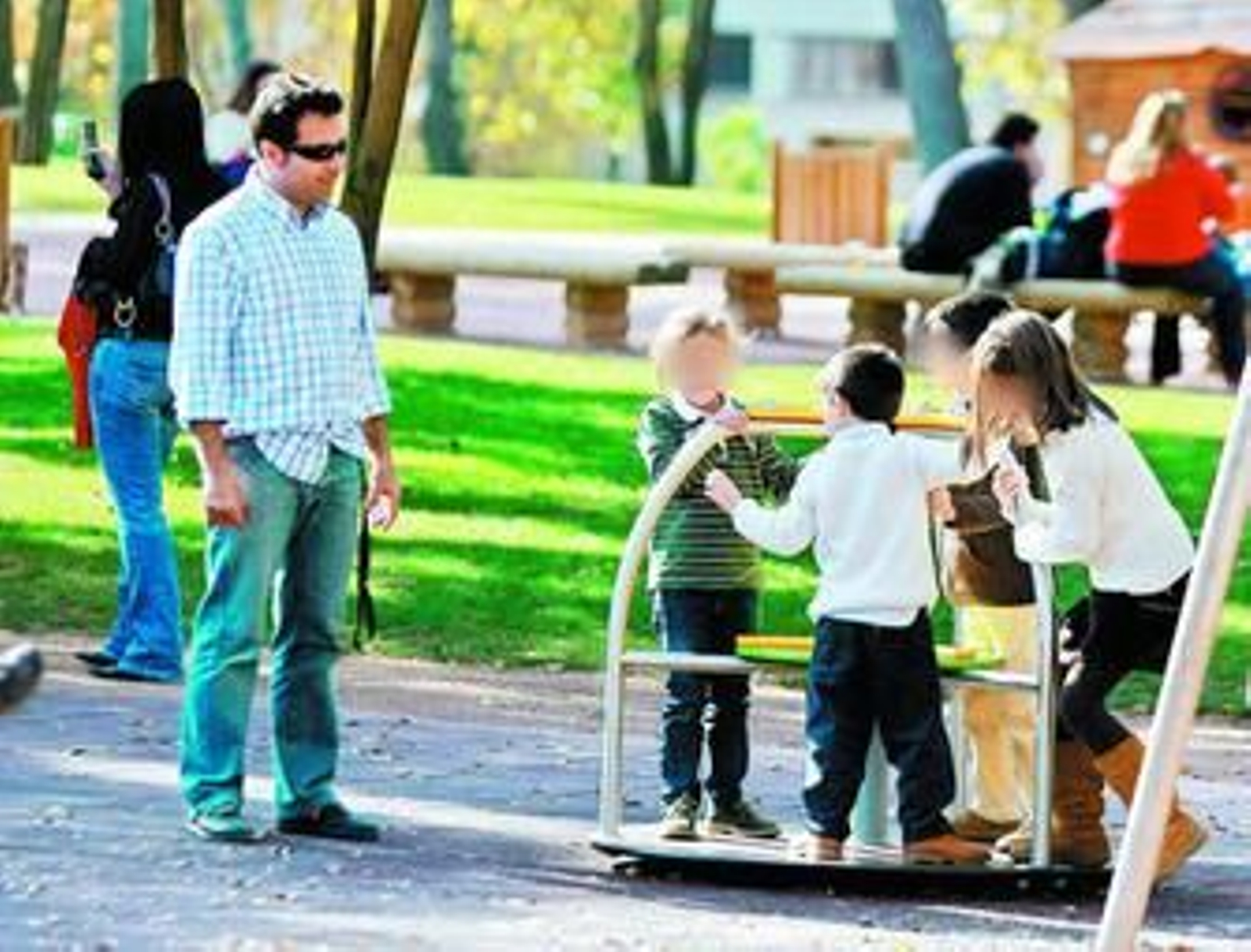 Un hombre observa a varios niños jugar en la zona recreativa de un parque público. Un hombre observa a varios niños jugar en la zona recreativa de un parque público.