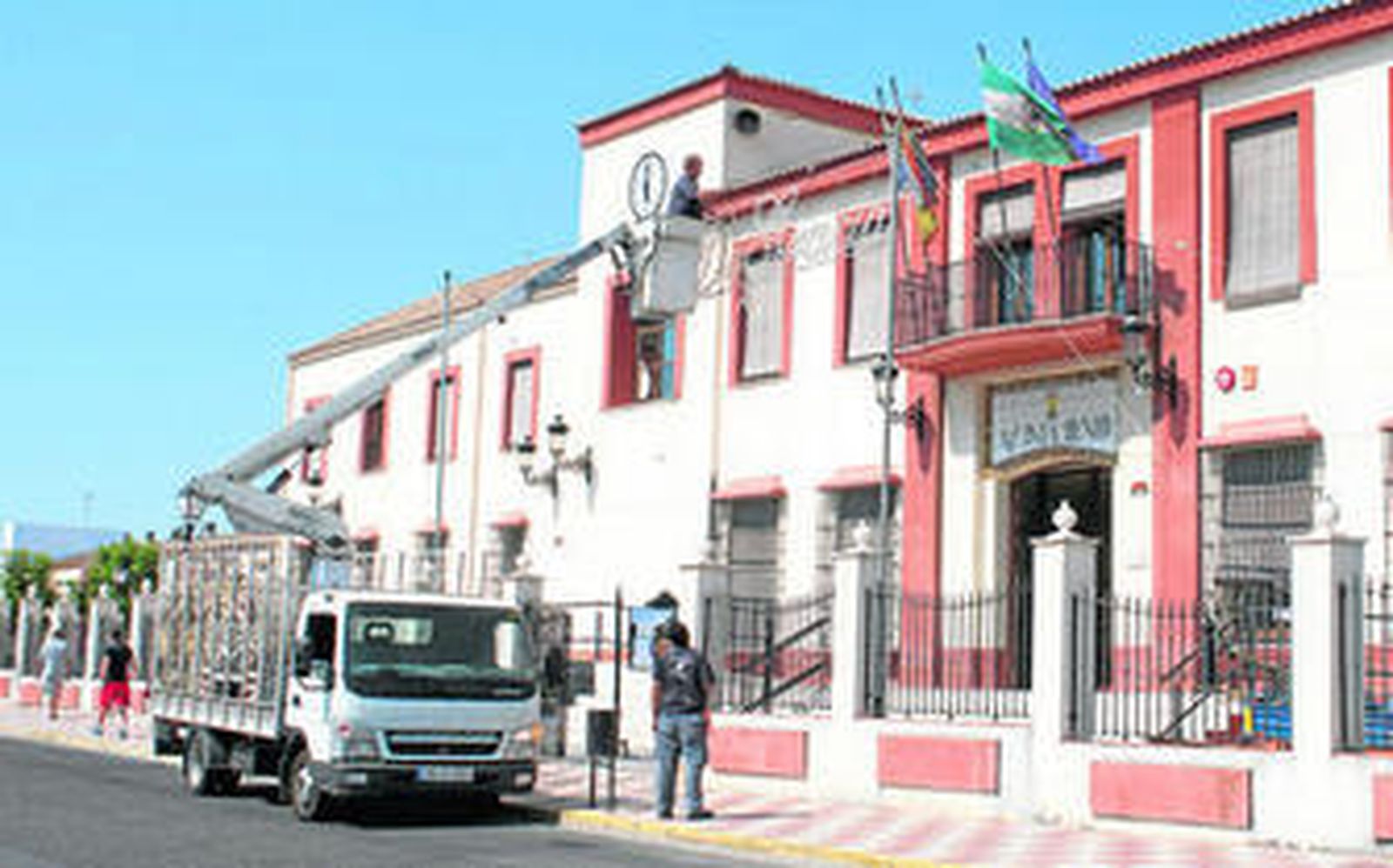 Varios operarios colocando, ayer, arcos de luces ante el Ayuntamiento de Gelves, que recupera su feria como fiesta patronal tras la suspensión de 2012.