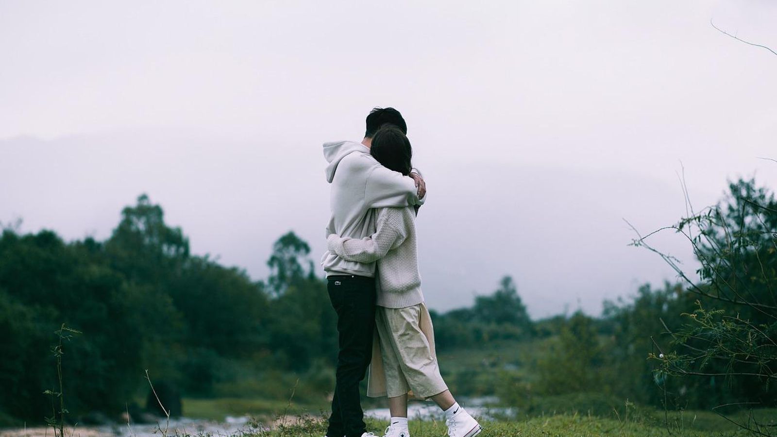 Una pareja se abraza en medio de un paraje natural.
