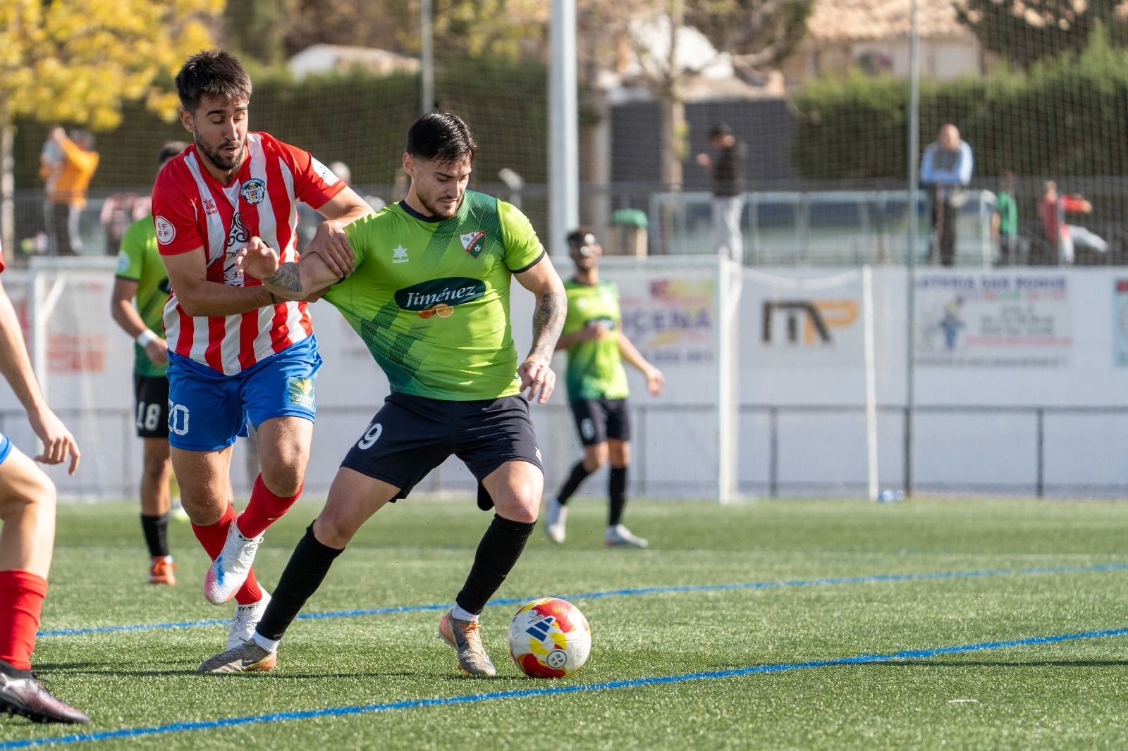 Un futbolista del Huétor Vega protegiendo el balón ante la presión de un futbolista del Porcuna.