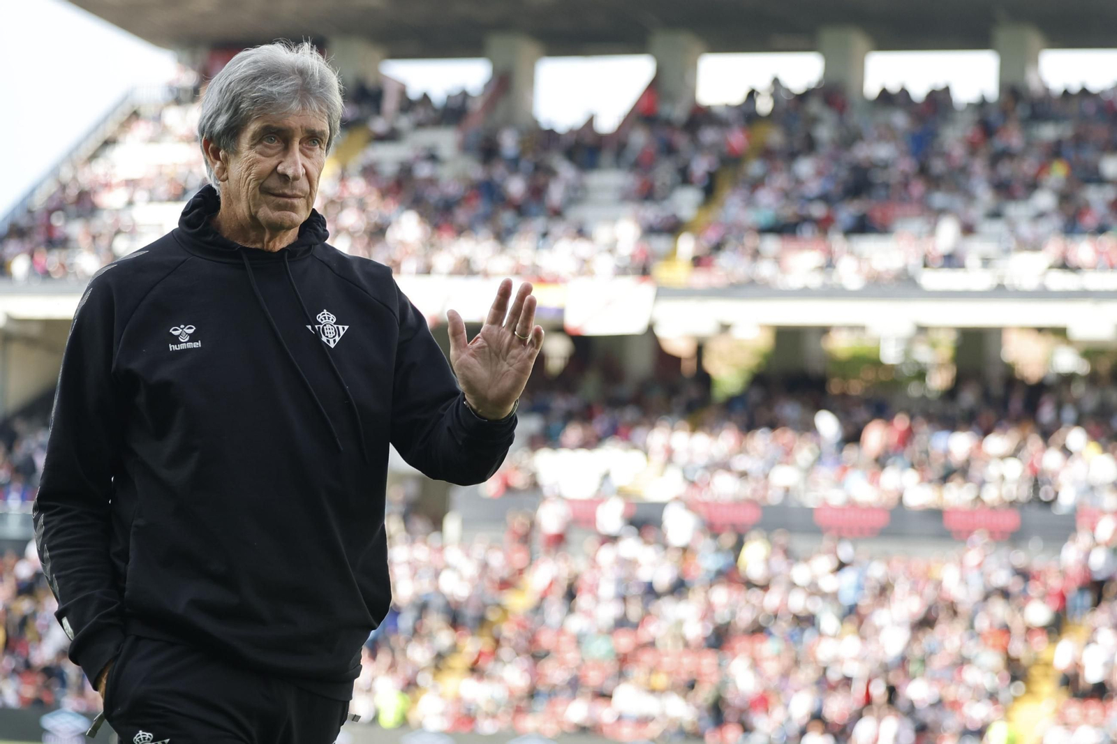 Manuel Pellegrini saluda a hinchas béticos a la llegada al banquillo para dar comienzo el partido de Vallecas.
