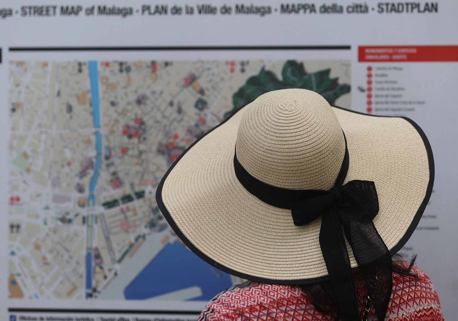 Una turista, que se protege del sol con un sombrero, observando un plano de Málaga.