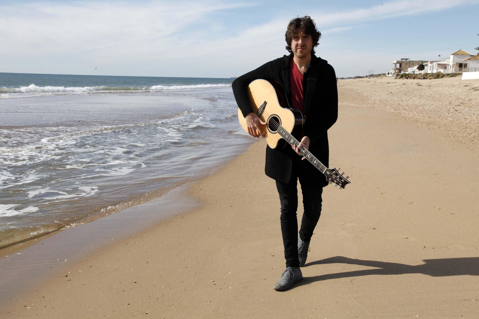 El cantautor onubense Alejandro Rivera, guitarra en mano en la playa.