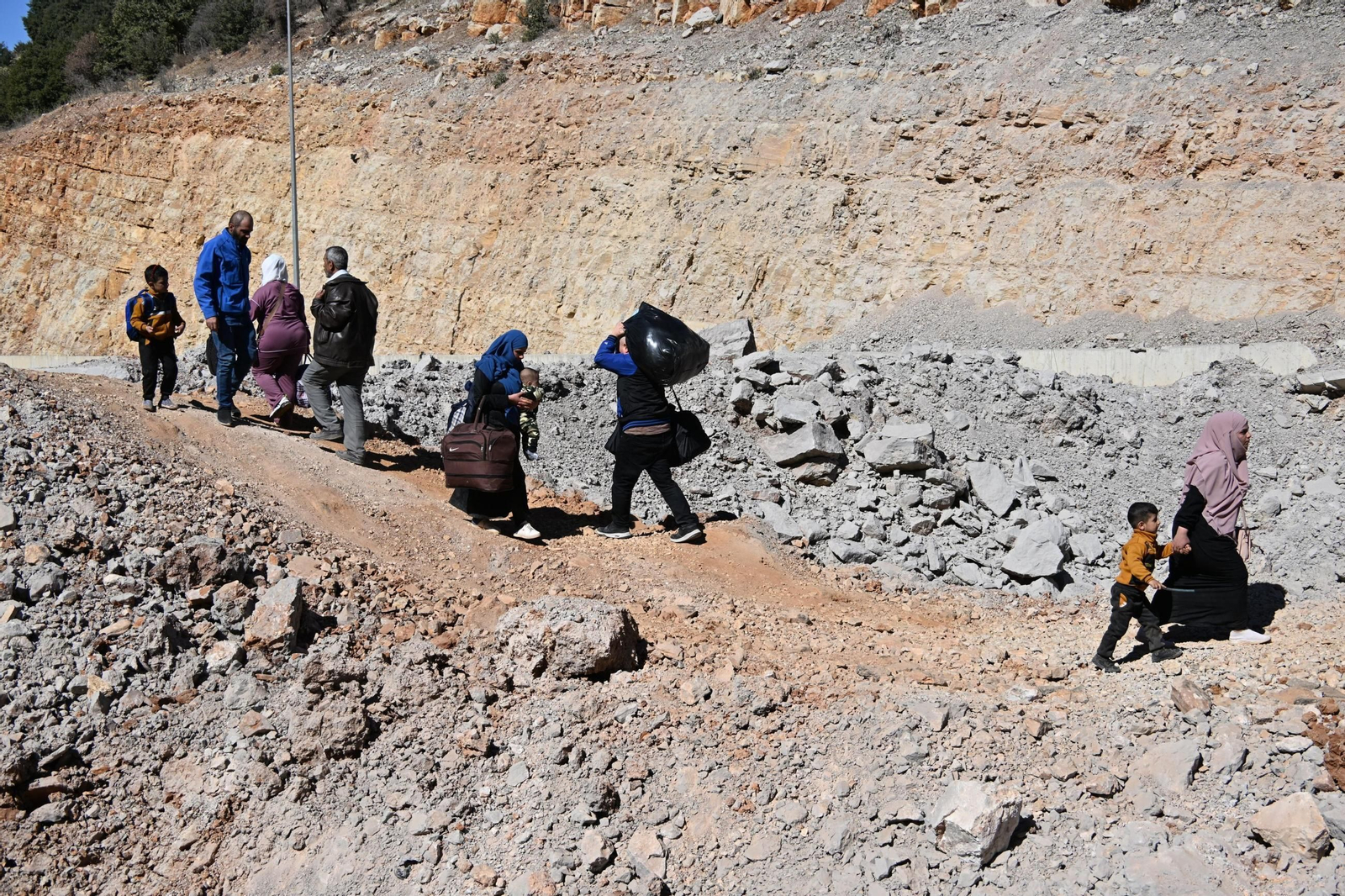 Un grupo de personas cargadas con sus pertenencias cruzan el destrozado paso fronterizo de Masnaa desde el Líbano hacia Siria.