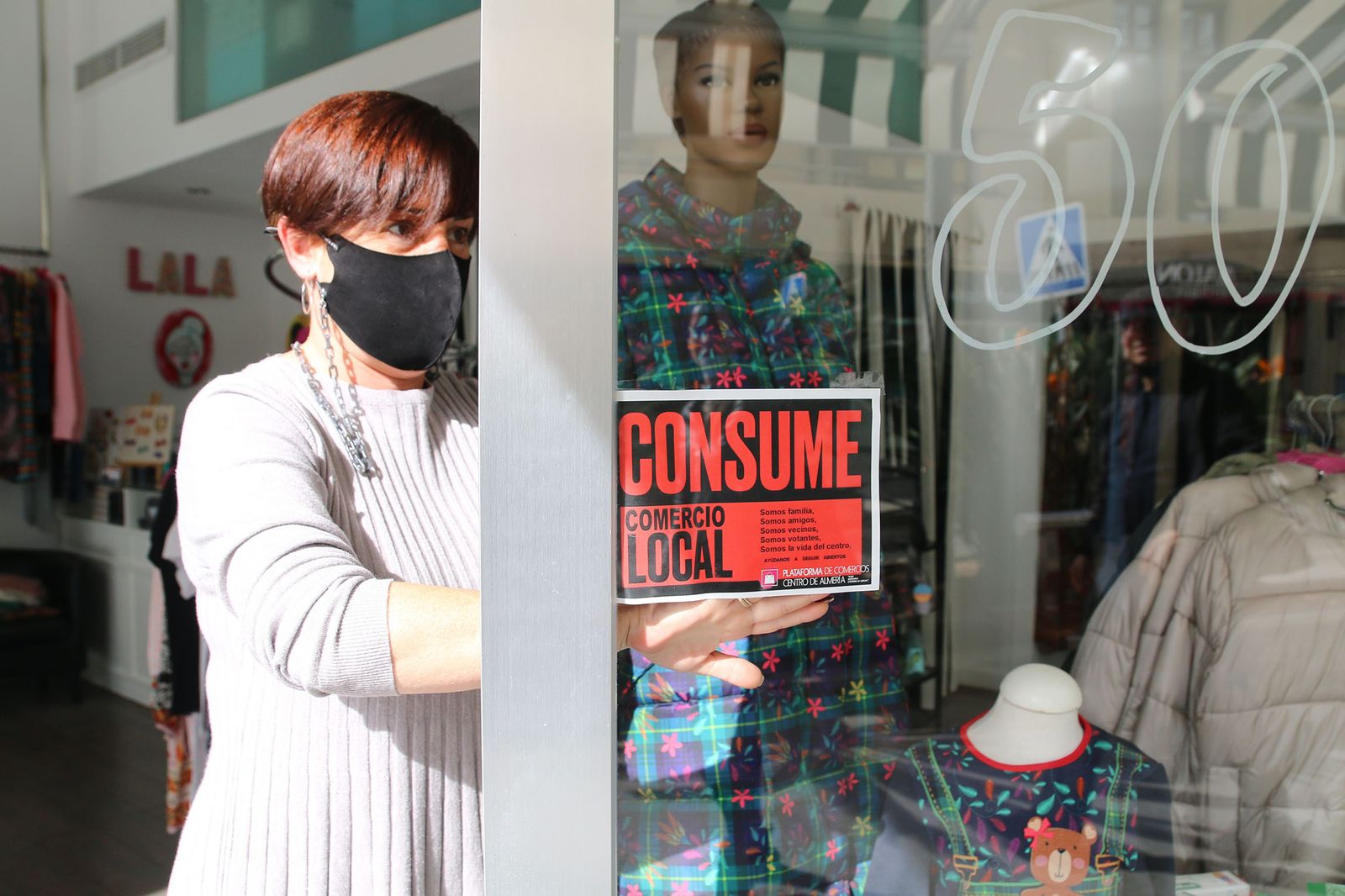 Una comerciante del centro de Almería coloca en su tienda el cartel de “consume comercio local”