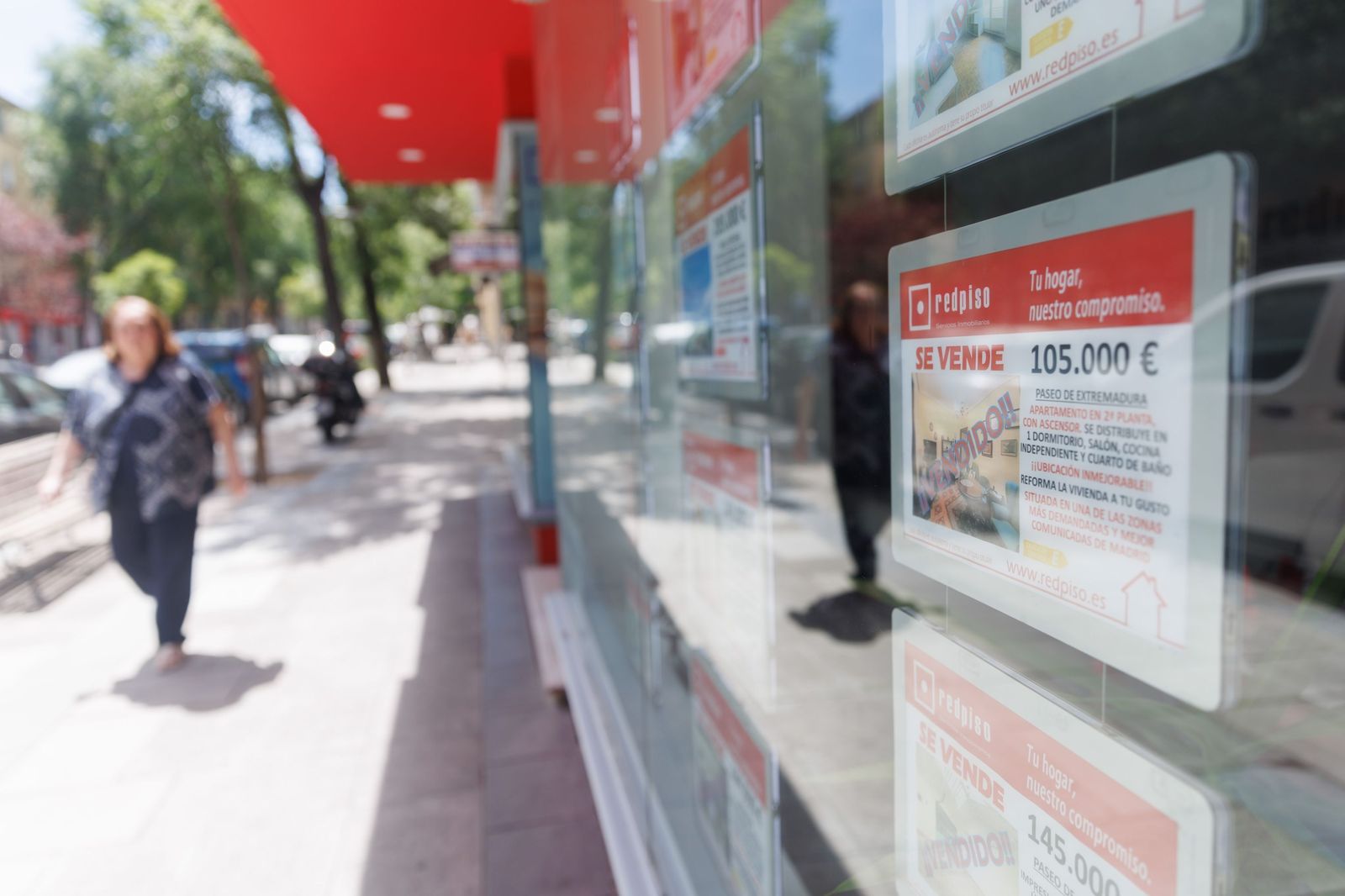 Una mujer camina junto a una inmobiliaria en la que se anuncian viviendas puestas a la venta.