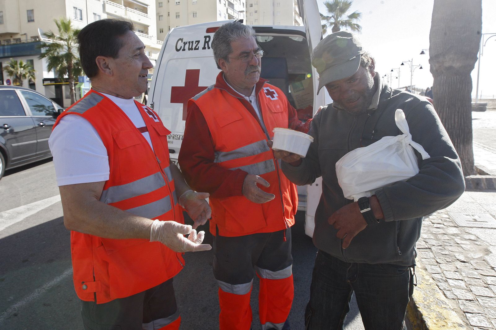 Voluntarios de Cruz Roja entregando ayer alimentos a Juan Carlos Bacalleda en el Paseo Marítimo.
