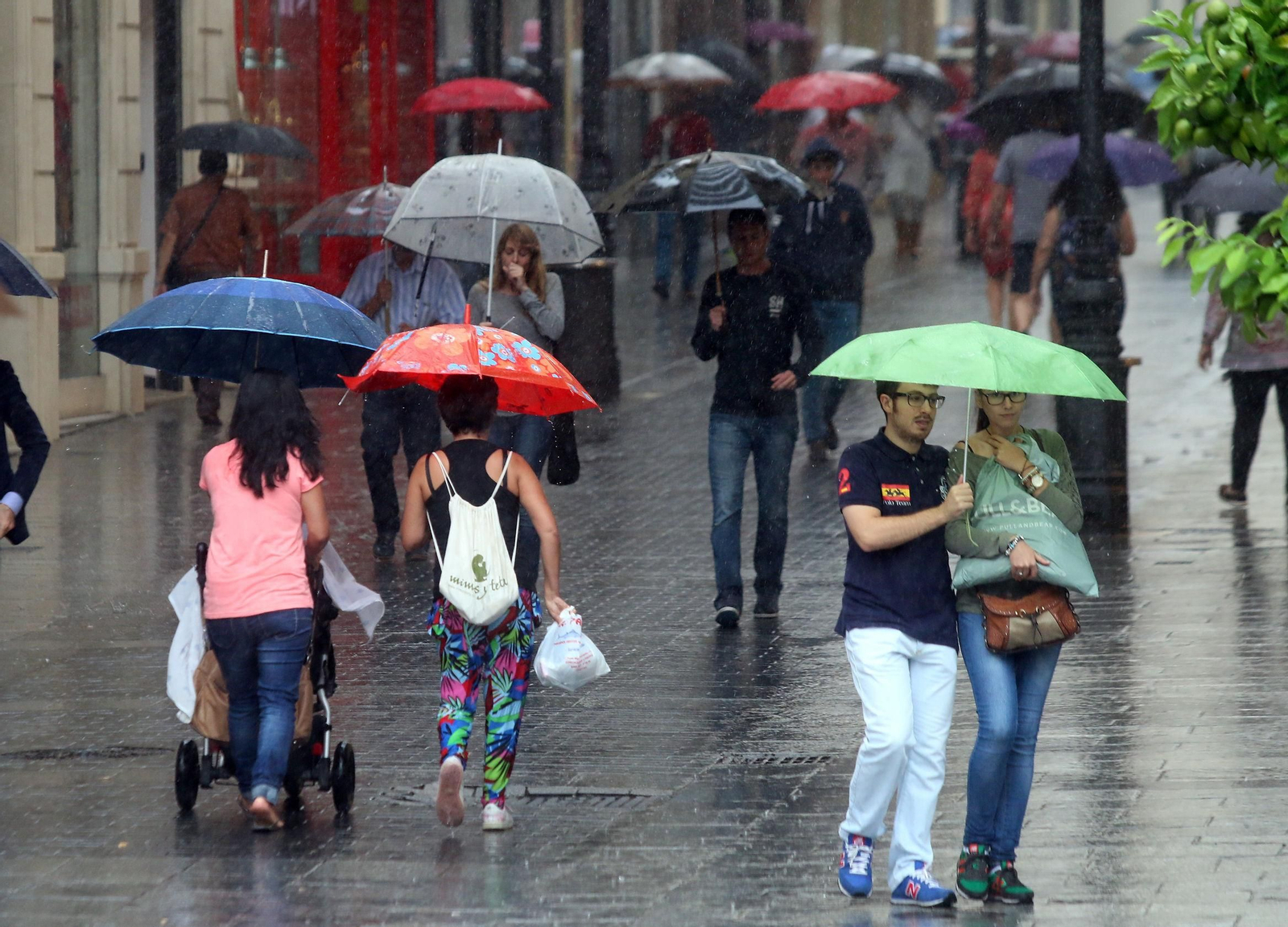 Numerosas personas en el centro de Córdoba pasean bajo la lluvia.