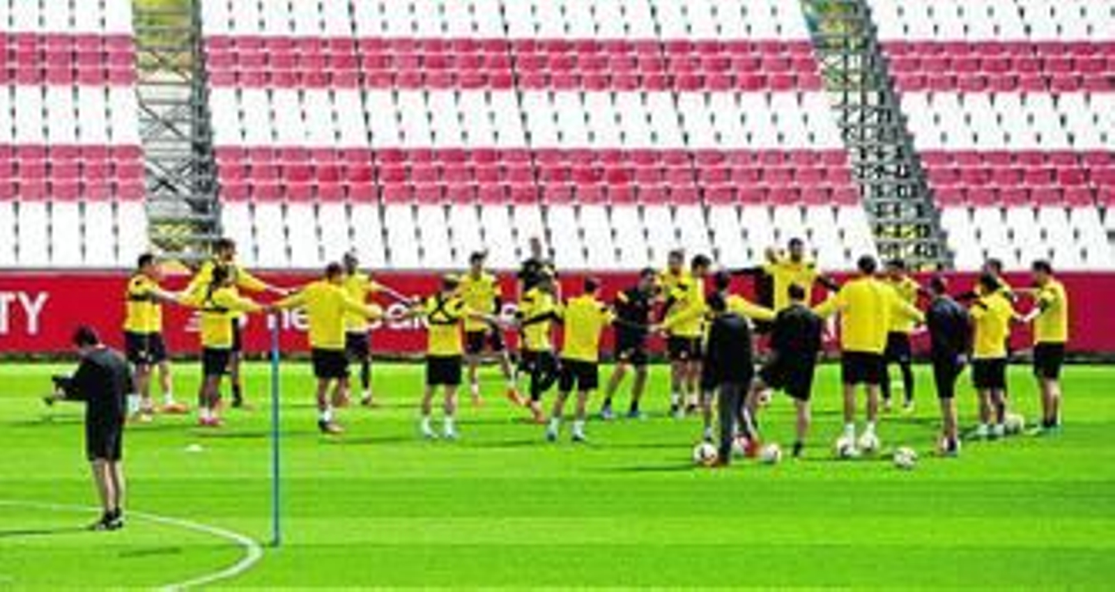 La plantilla sevillista, cogida de las manos durante un entrenamiento reciente. Emery, mientras consulta sus notas.