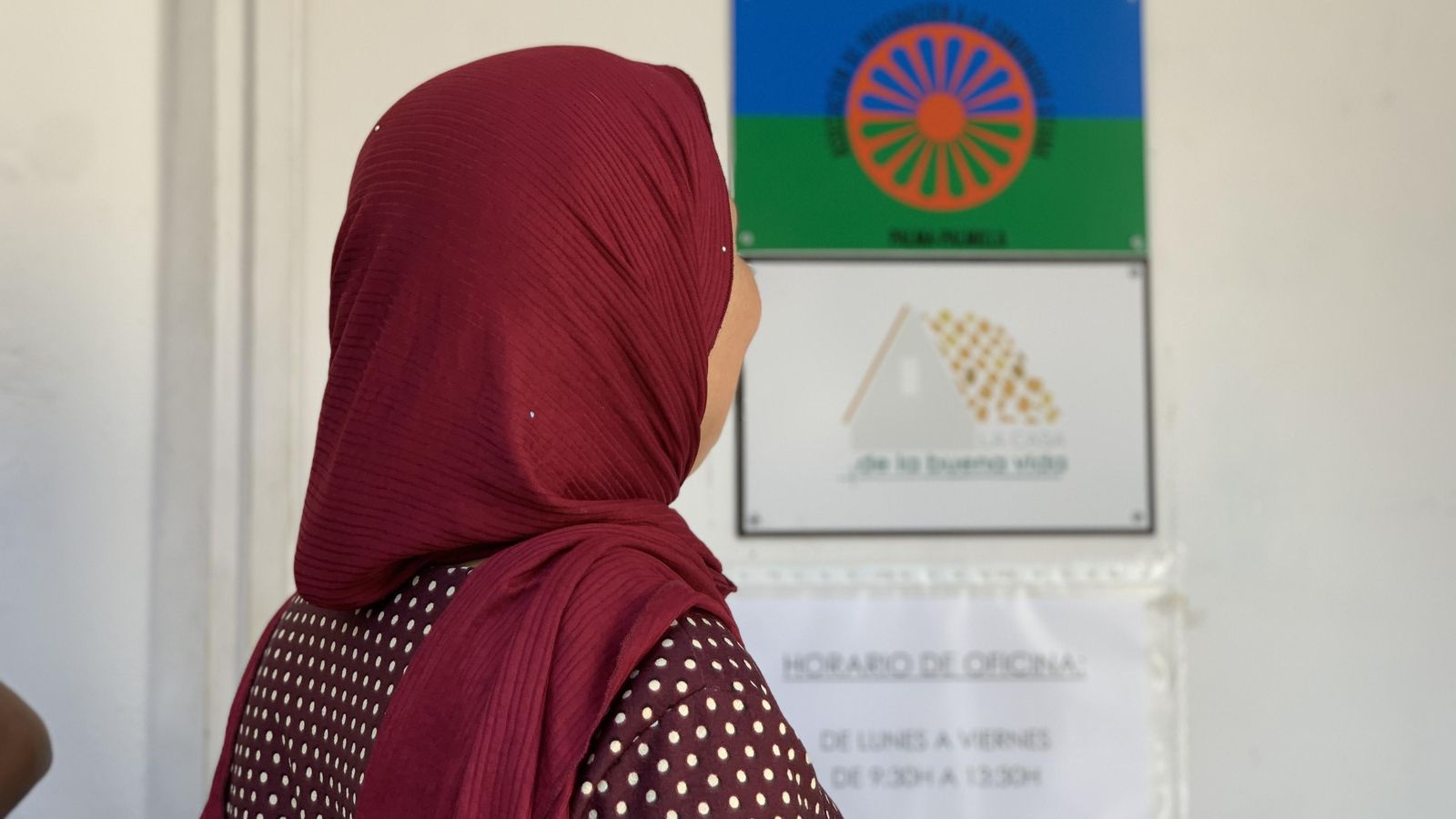Una mujer musulmana esperando para recibir alimentos; de fondo, la bandera gitana.