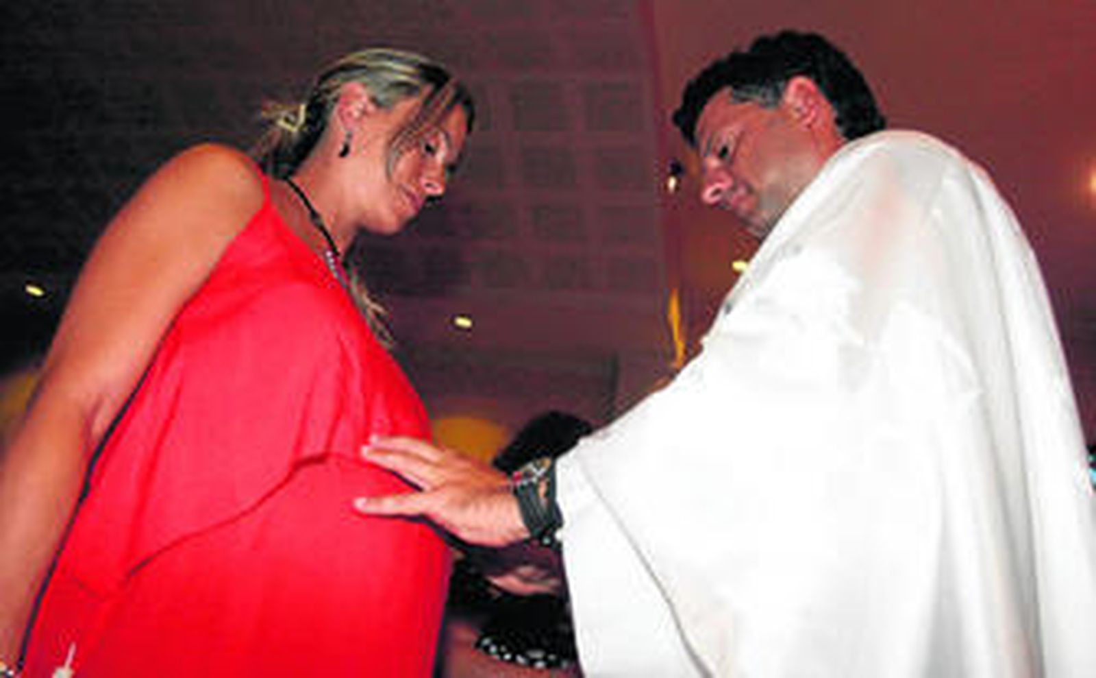 El párroco impone las manos sobre el vientre de la madre para bendecir a su hijo.