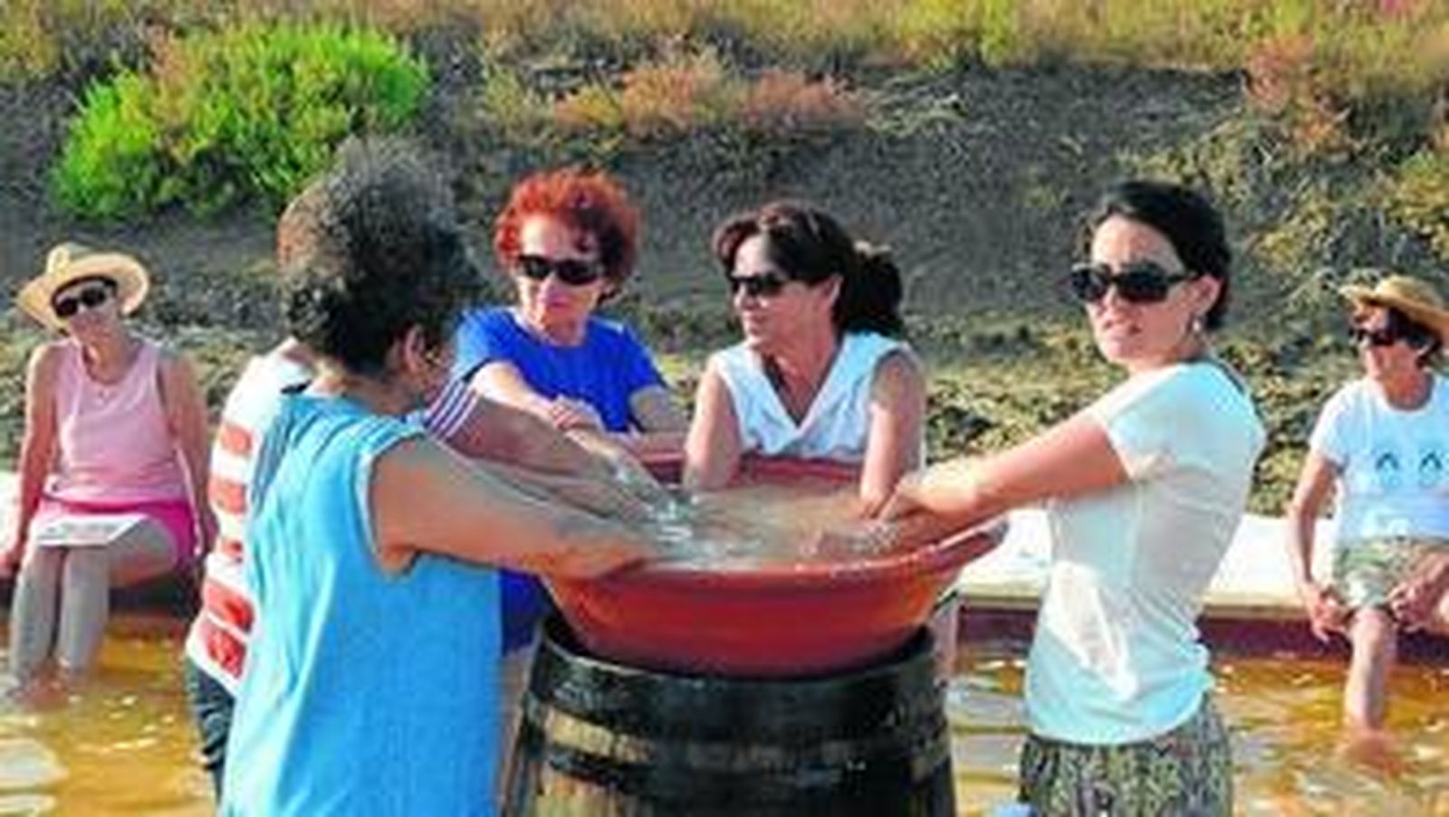 Un grupo de mujeres meten las manos en una tinaja con sal marina.