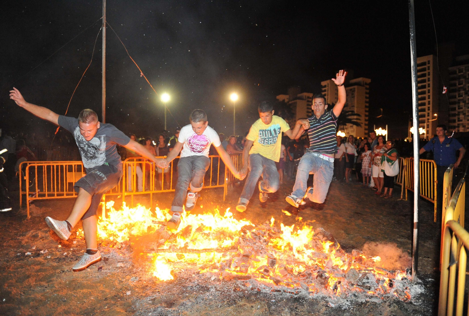Varios jóvenes saltan juntos una hoguera en la playa en la Noche de San Juan.