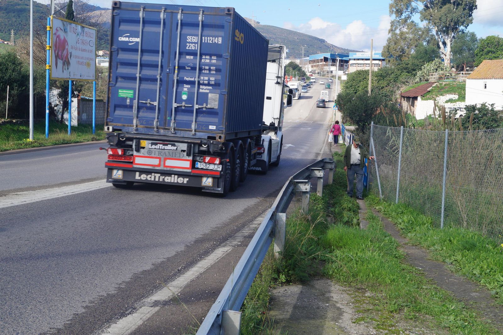 Dos personas caminan por el arcén, al paso de un camión en la entrada al polígono Cortijo Real, que da acceso a la izquierda a Los Guijos.