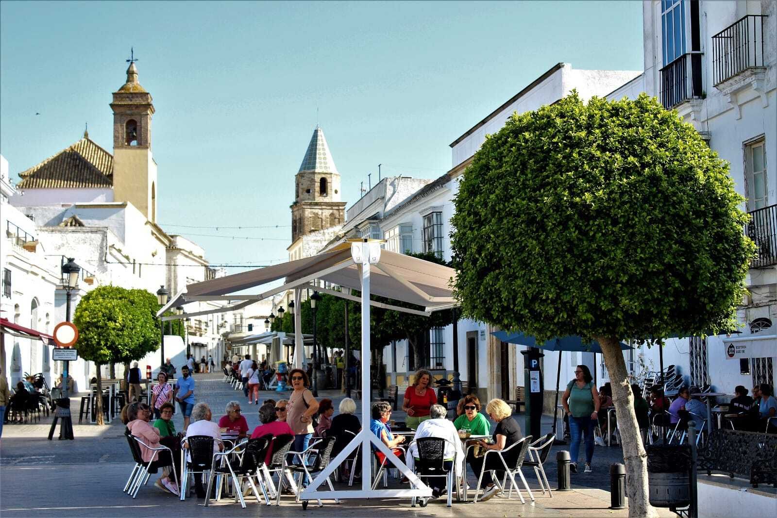 Una terraza en el límite entre la Plaza España y la calle San Juan en Medina, con muchas mujeres desayunando.