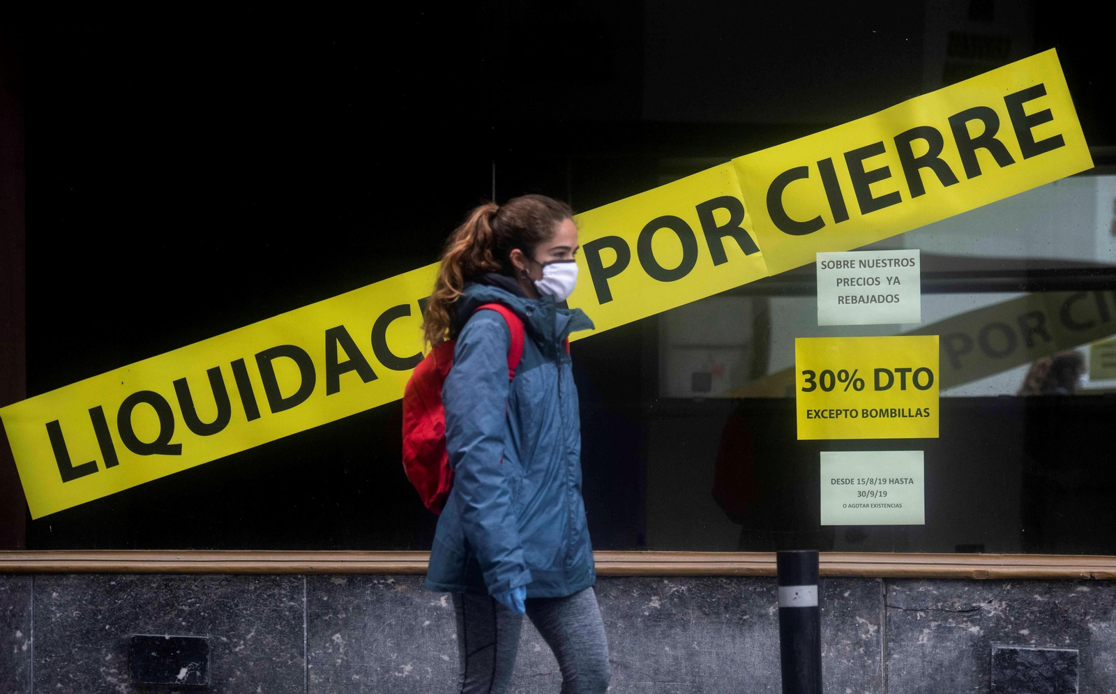 Una joven pasa delante de una tienda cerrada en Córdoba.