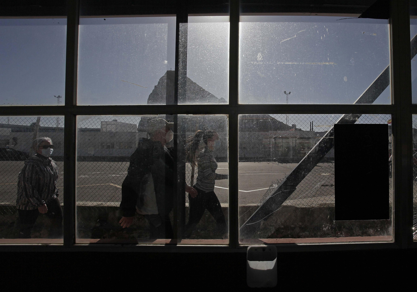 Varias personas cruzan el paso entre La Línea y Gibraltar con el Peñón al fondo.