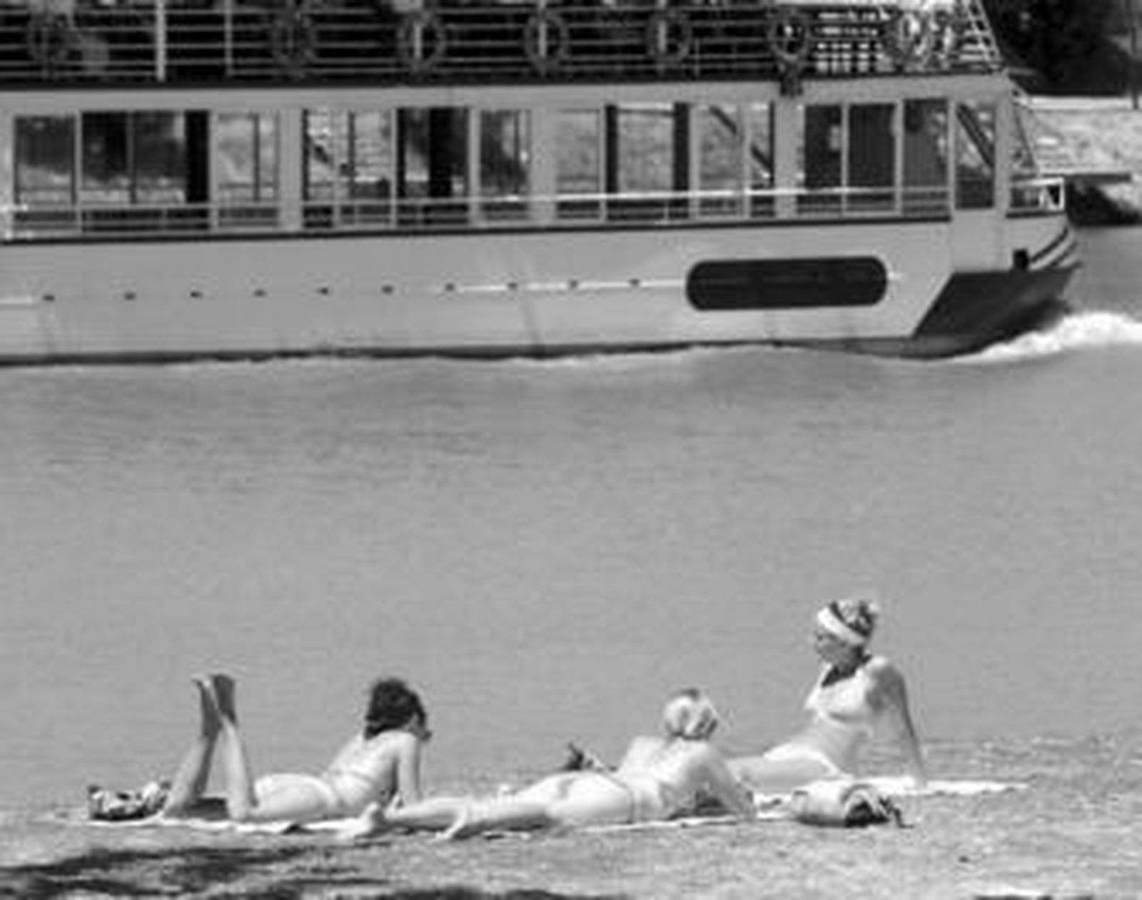 Un grupo de chicas toma el sol en el césped de la orilla del Guadalquivir.