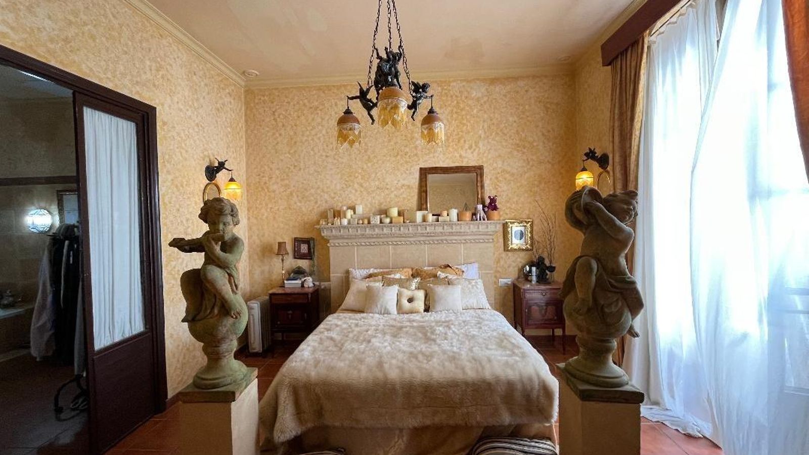 La cama con el  cabecero de mampostería y el piecero con una pareja de esculturas.