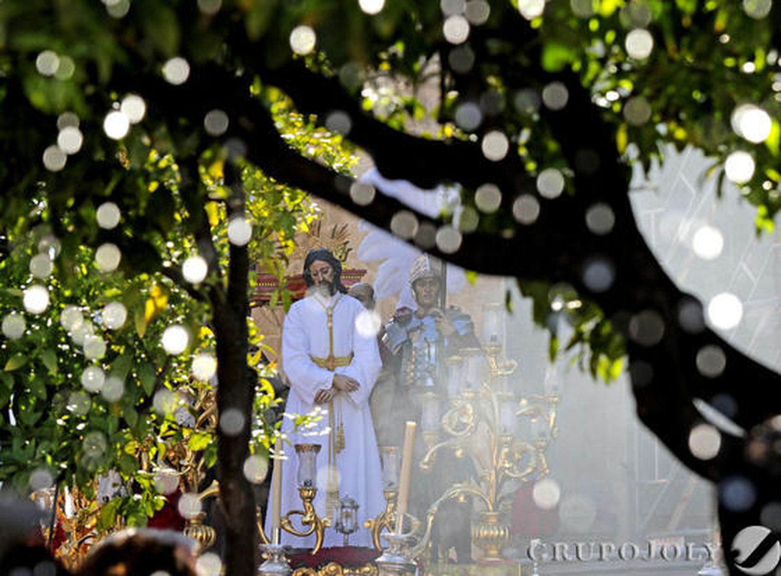 El misterio de Nuestro Padre Jesús del Consuelo se vislumbra entre las ramas de los naranjos situados en torno a la fuente de Santiago.

Foto: Miguel Angel Gonzalez