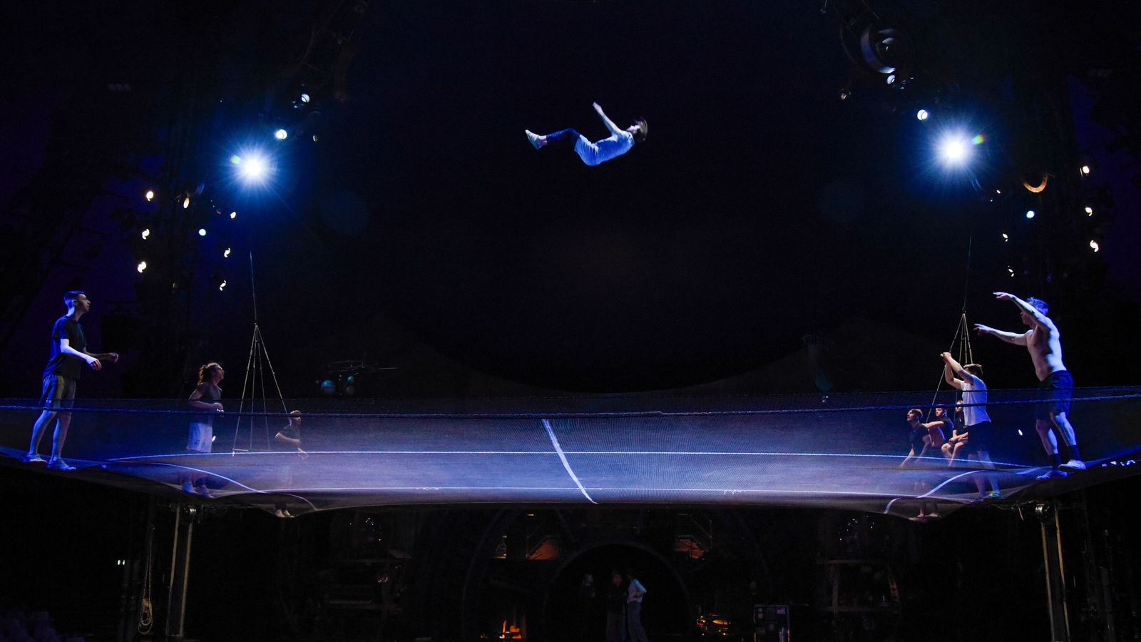 Siete artistas practican el número de Acro Net en el que una red inmensa queda suspendida sobre el escenario.