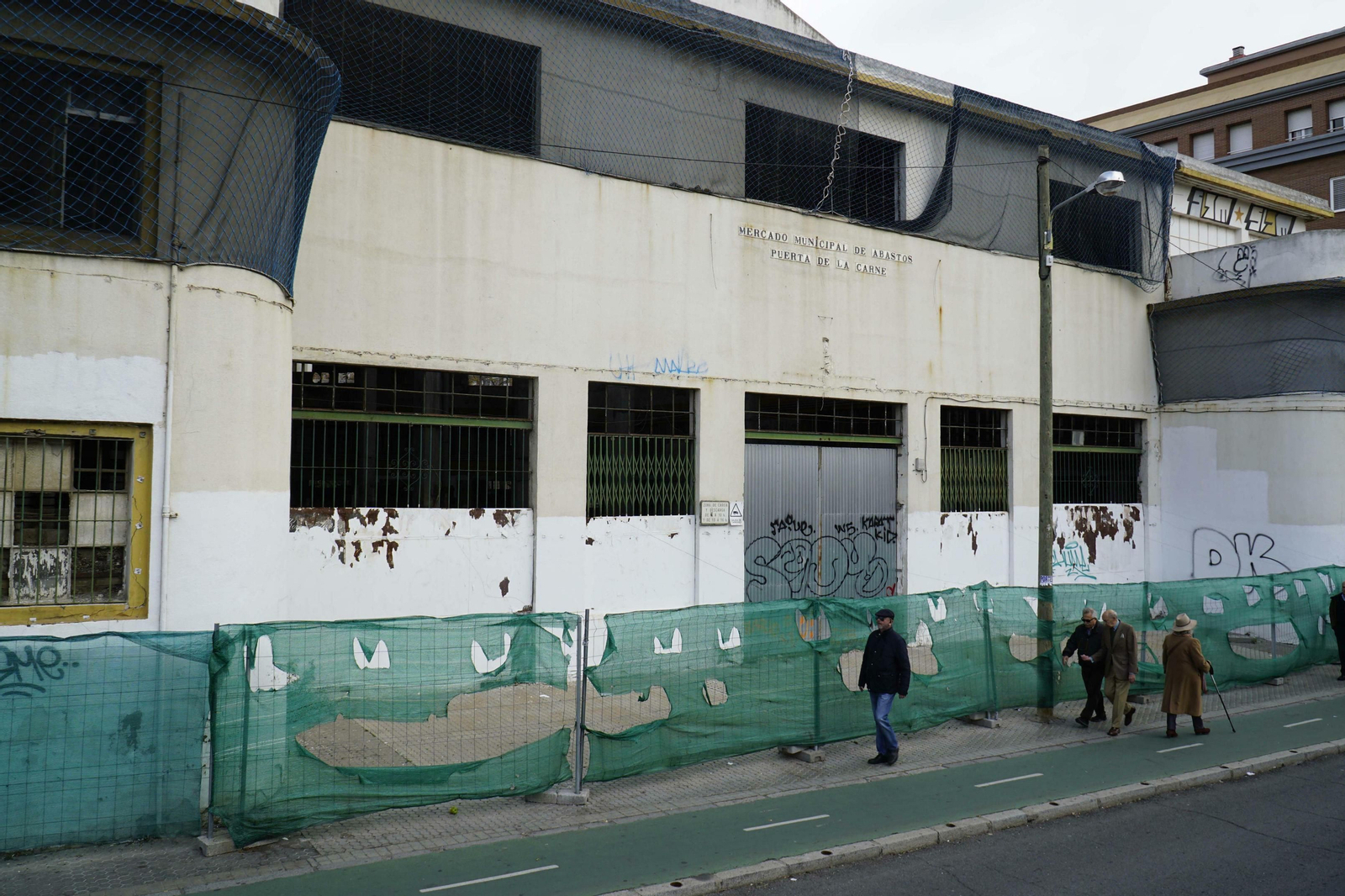Varias personas caminan por la acera junto a la entrada principal del Mercado de la Puerta de la Carne.
