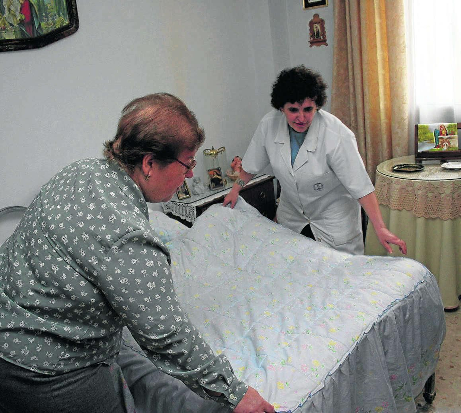 Una trabajadora de Ayuda a Domicilio echa una mano a una mujer para hacer la cama.