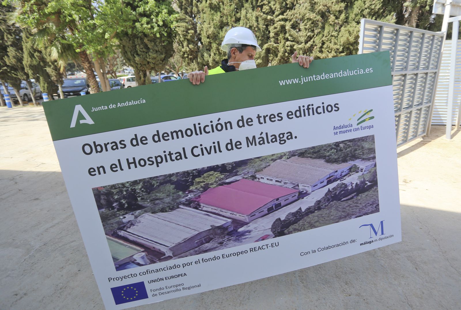 Un operario traslada el cartel en el que se indica la demolición del antiguo hospital para construir el nuevo.