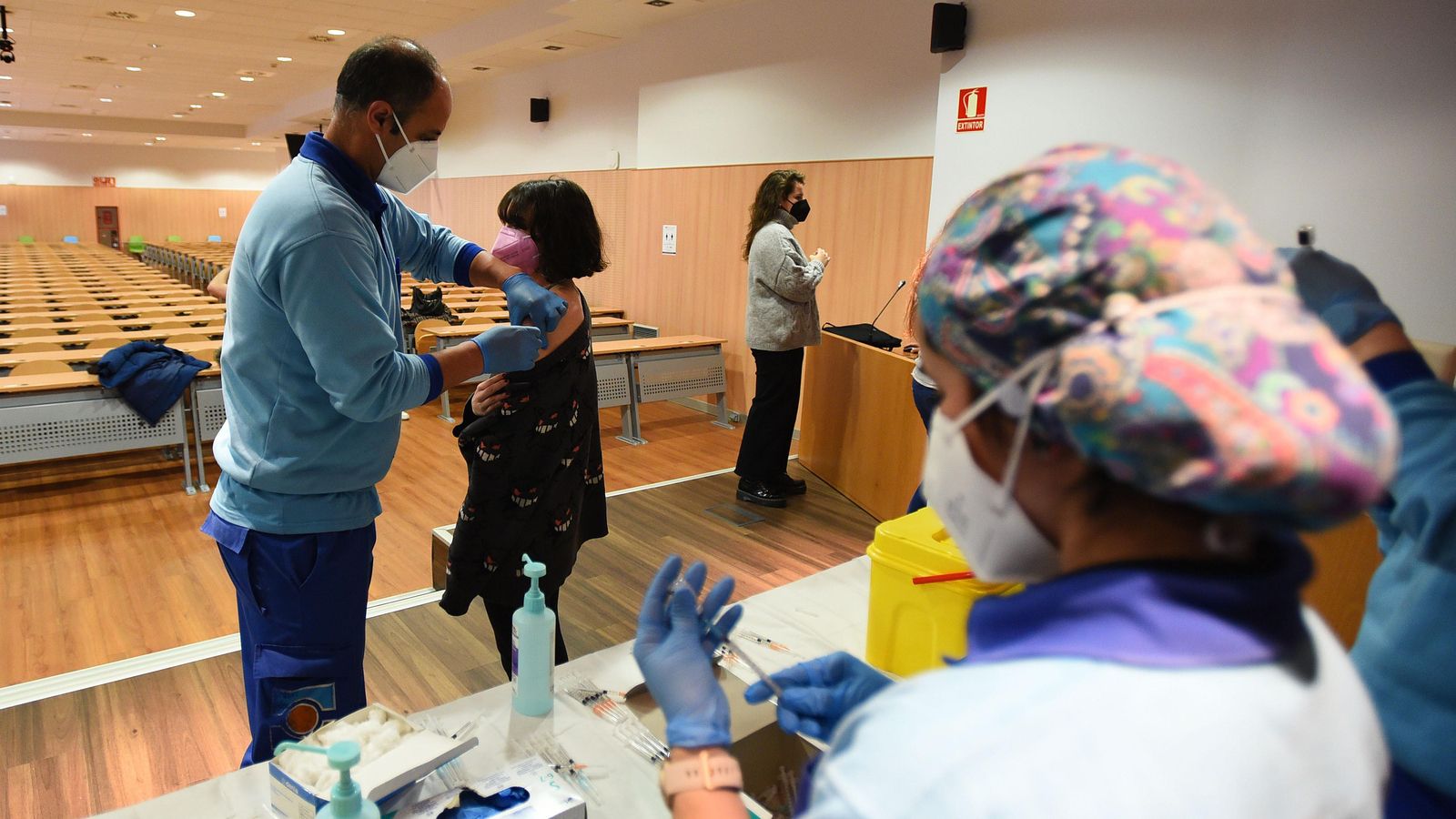 Una profesional  prepara una dosis mientras otro sanitario inyecta la vacuna.