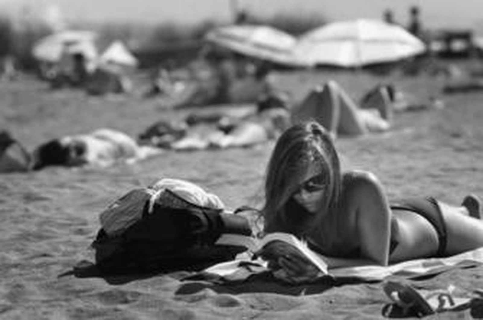 Una joven lee un libro mientras se encuentra tomando el sol en una playa.