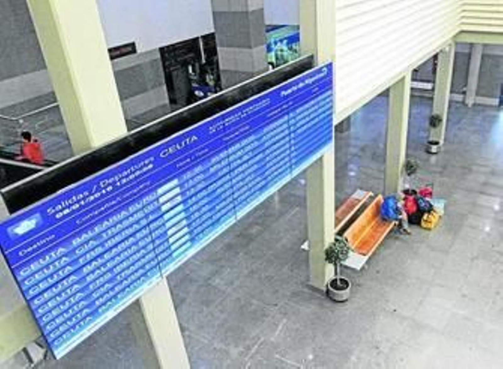 Una persona espera en la estación marítima de Algeciras bajo el panel informativo de los ferris a Ceuta.