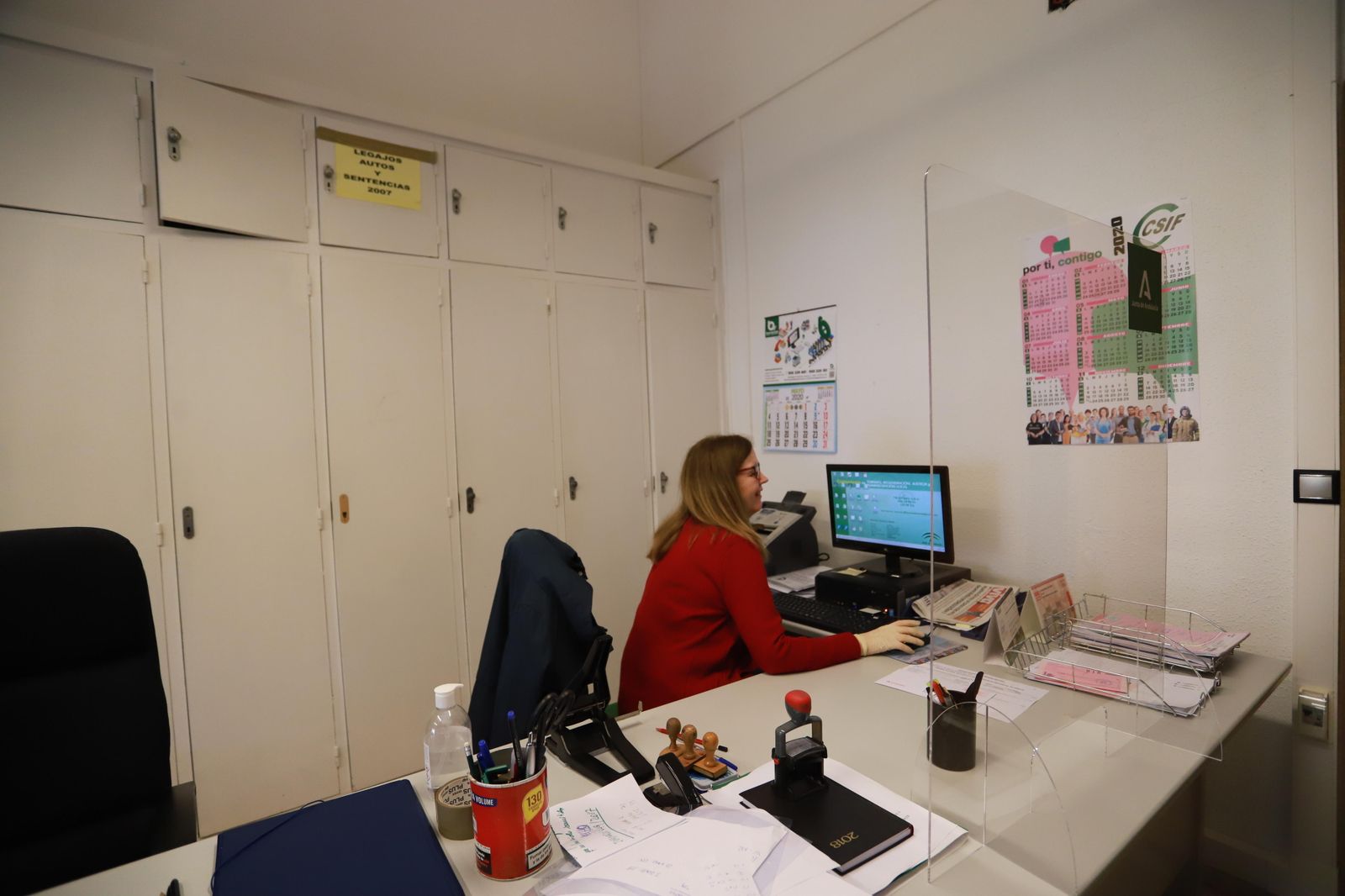 Una funcionaria del Palacio de Justicia de Huelva trabaja protegida por una mampara.