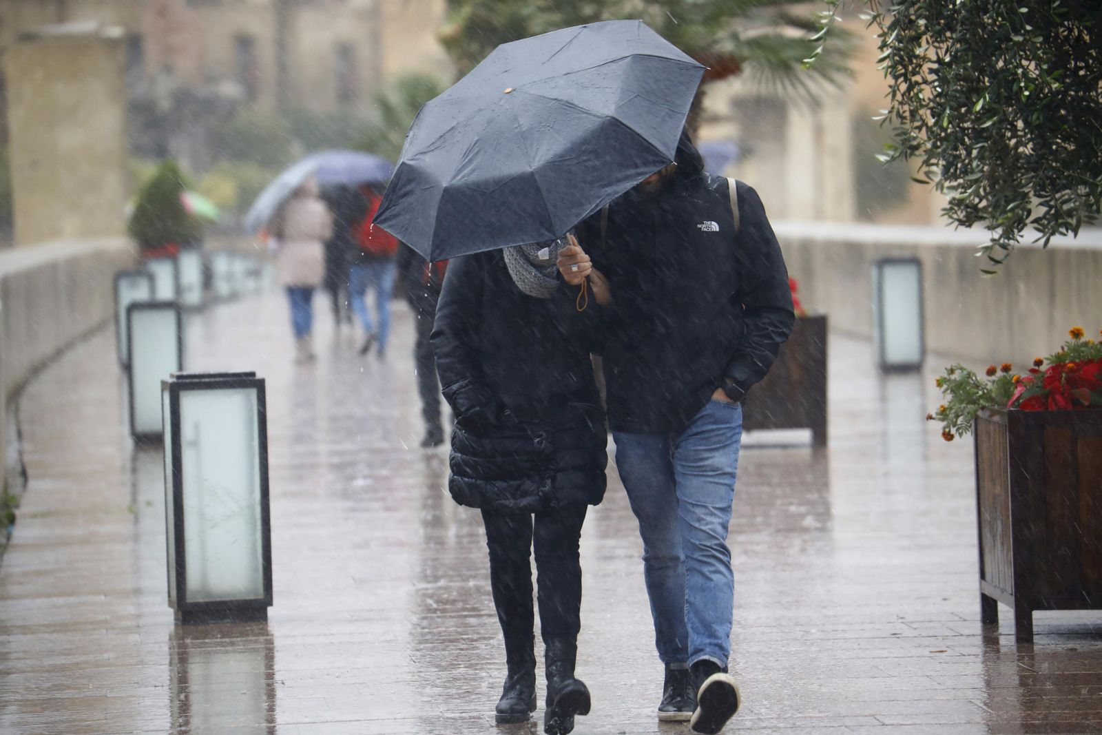 Dos personas caminan por el Puente Romano de Córdoba bajo la lluvia.