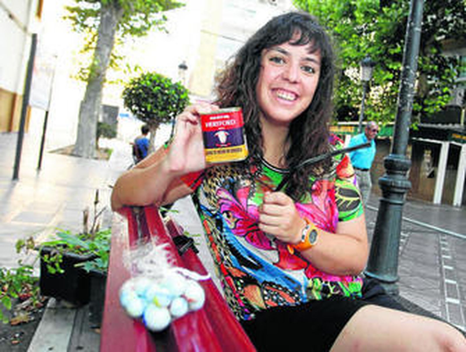 María Ortega posa con una lata de 'carne combí', un 'liquirbá' y una bolsa de 'meblis' en un banco del centro de La Línea.